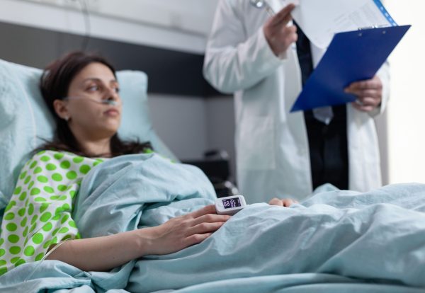 woman-hospital-bed-with-pulse-oximeter-finger-showing-low-oxygen-saturation-listening-doctor-reading-lab-results-from-clipboard-patient-with-nasal-cannula-recieving-diagnosis-results